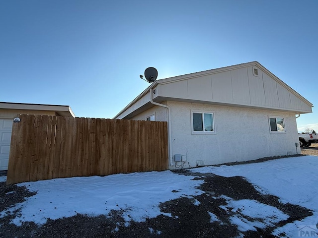 snow covered property featuring a garage, fence, and stucco siding