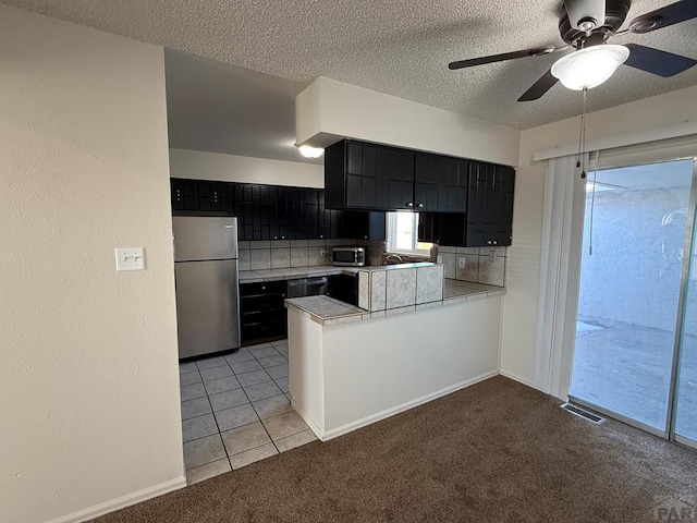 kitchen with stainless steel appliances, light countertops, decorative backsplash, dark cabinets, and a peninsula