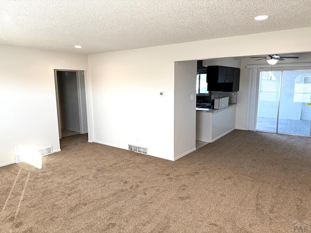 unfurnished living room with a textured ceiling, carpet flooring, visible vents, and a ceiling fan