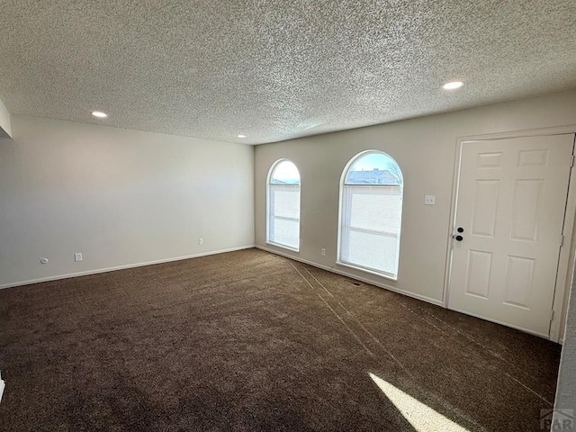 interior space featuring dark colored carpet, a textured ceiling, baseboards, and recessed lighting