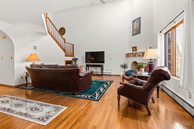 living room with a baseboard heating unit, hardwood / wood-style floors, arched walkways, a baseboard radiator, and a towering ceiling