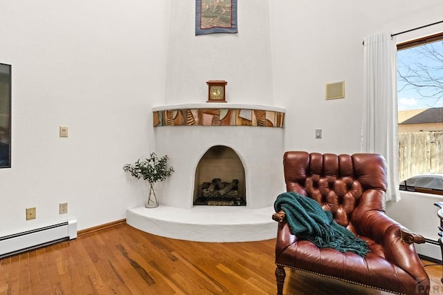 sitting room featuring wood finished floors, visible vents, baseboards, a fireplace with raised hearth, and a baseboard heating unit