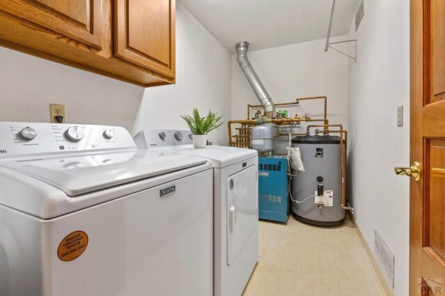 clothes washing area with visible vents, washing machine and dryer, gas water heater, cabinet space, and baseboards