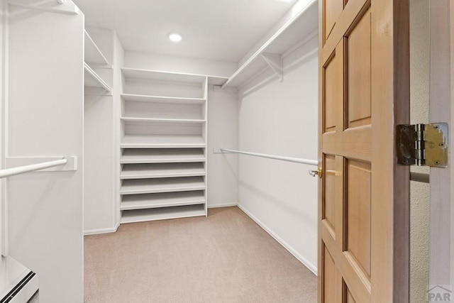 spacious closet with light colored carpet and a baseboard radiator