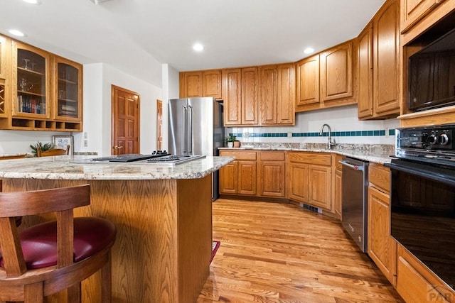 kitchen featuring light wood-type flooring, black appliances, a sink, a breakfast bar area, and light stone countertops