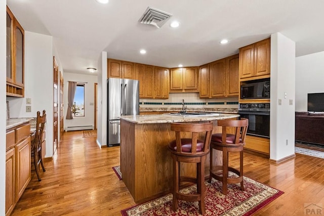 kitchen with light stone counters, visible vents, a baseboard radiator, black appliances, and light wood-type flooring