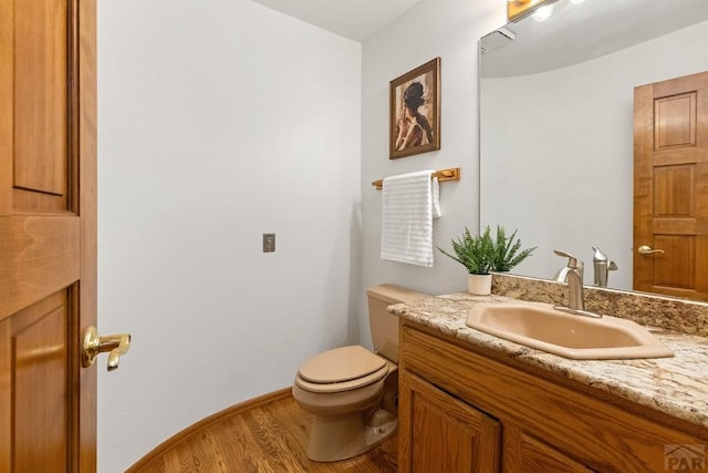 bathroom with vanity, toilet, wood finished floors, and baseboards