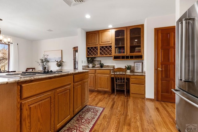 kitchen featuring glass insert cabinets, light stone countertops, cooktop, light wood-style flooring, and high quality fridge