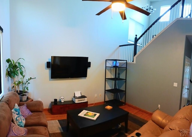 living room featuring stairs, ceiling fan with notable chandelier, a towering ceiling, and wood finished floors