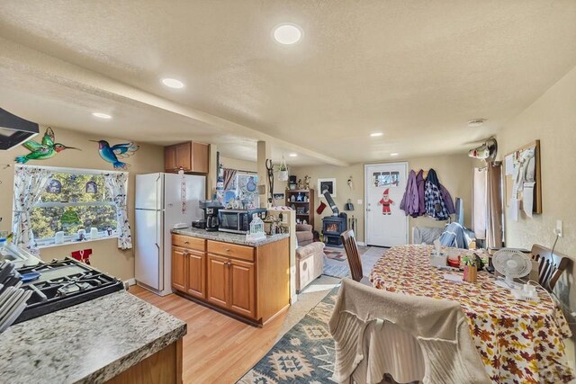 kitchen featuring brown cabinets, stainless steel microwave, light wood-style floors, freestanding refrigerator, and open floor plan