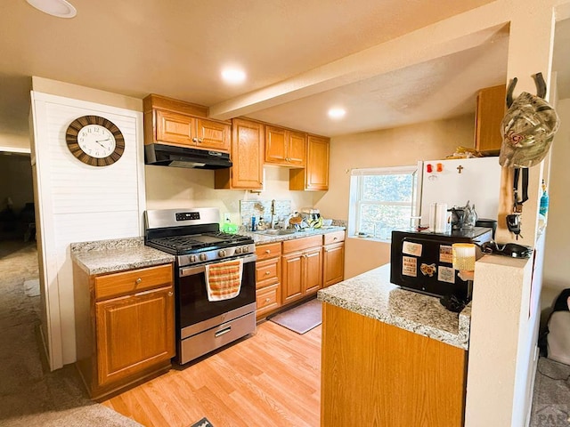 kitchen with freestanding refrigerator, stainless steel range with gas stovetop, a sink, light wood-type flooring, and under cabinet range hood