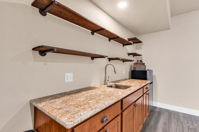 kitchen featuring dark wood-style floors, open shelves, brown cabinetry, a sink, and light stone countertops