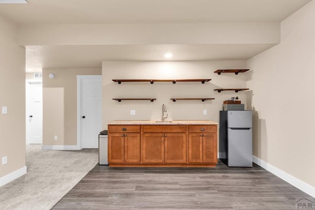 kitchen with a sink, light countertops, open shelves, and freestanding refrigerator