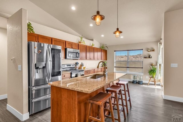 kitchen with decorative light fixtures, a center island with sink, appliances with stainless steel finishes, a sink, and a kitchen bar