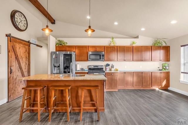 kitchen featuring a barn door, an island with sink, appliances with stainless steel finishes, hanging light fixtures, and a sink