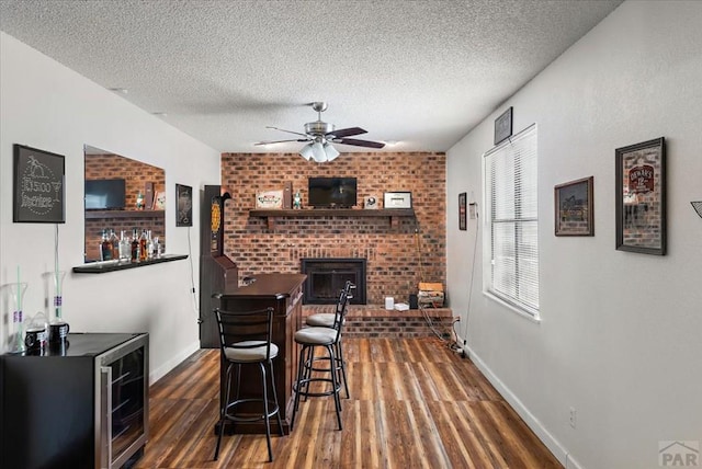 bar with dark wood-style floors, ceiling fan, a textured ceiling, and a brick fireplace