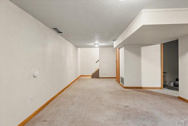 finished basement with carpet, visible vents, a textured ceiling, baseboards, and stairs