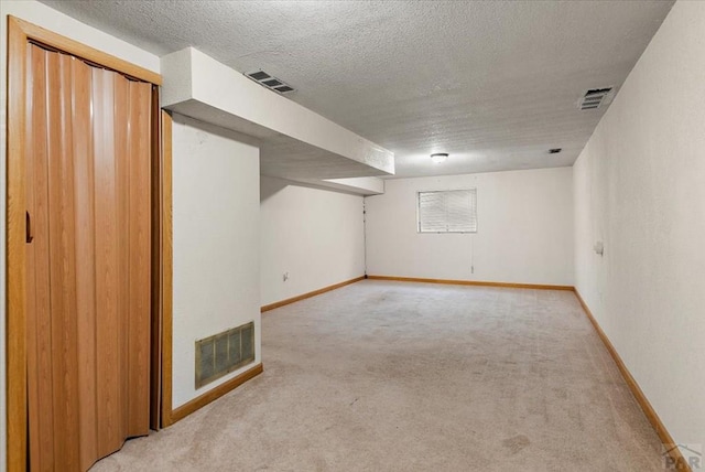 finished below grade area with light carpet, baseboards, visible vents, and a textured ceiling