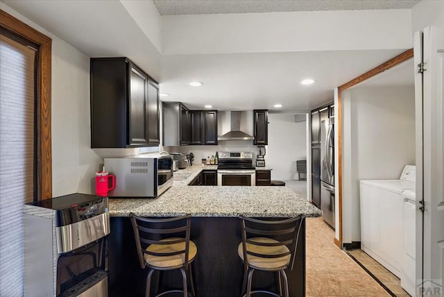 kitchen with wall chimney exhaust hood, a breakfast bar, a peninsula, stainless steel appliances, and recessed lighting