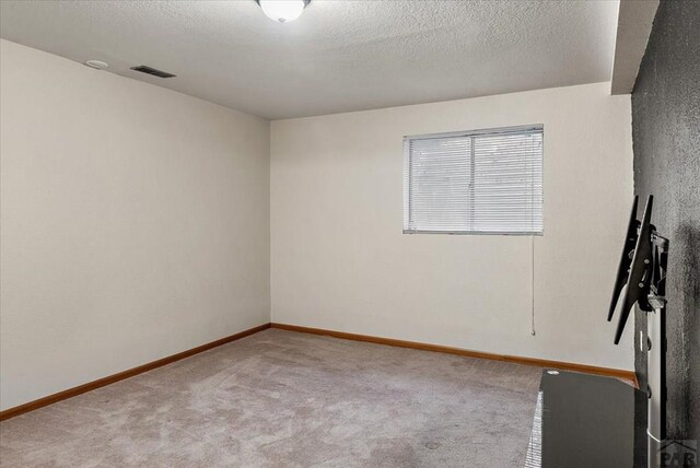 spare room featuring light carpet, baseboards, visible vents, and a textured ceiling