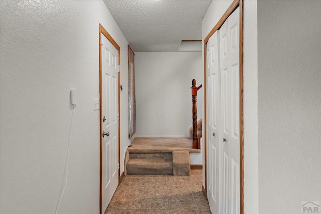 hall featuring a textured ceiling and baseboards