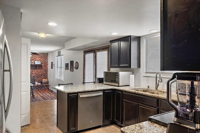 kitchen with a textured ceiling, light stone counters, stainless steel appliances, a peninsula, and a sink