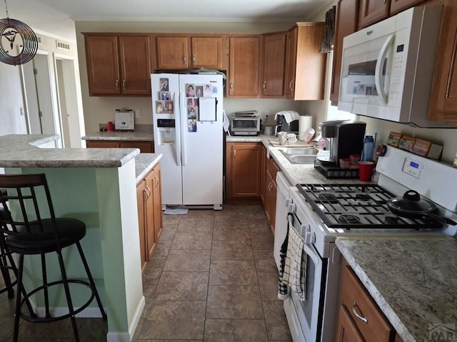 kitchen with brown cabinetry, white appliances, light countertops, and a kitchen breakfast bar