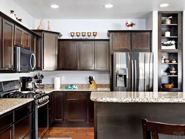 kitchen with stainless steel appliances, light wood-type flooring, dark brown cabinetry, and light stone counters