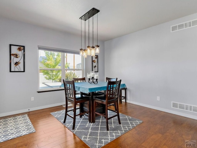 dining room with baseboards, wood finished floors, visible vents, and a notable chandelier