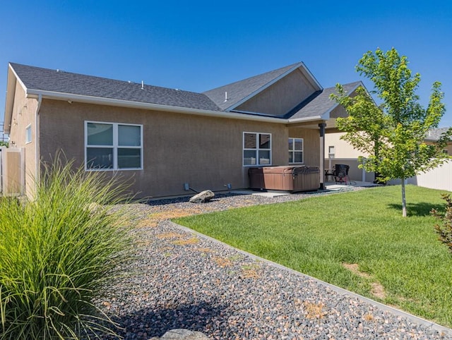 back of property featuring a lawn, stucco siding, fence, and a hot tub