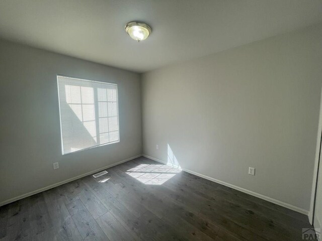 unfurnished room featuring dark wood-style floors, visible vents, and baseboards