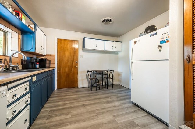 kitchen with white appliances, white cabinets, blue cabinets, light countertops, and a sink