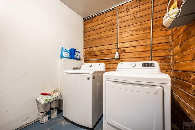 washroom featuring laundry area, separate washer and dryer, and wood walls