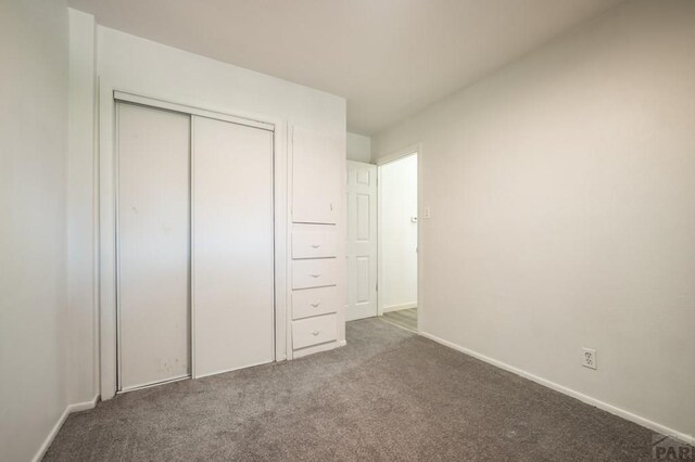 unfurnished bedroom featuring a closet, dark carpet, and baseboards