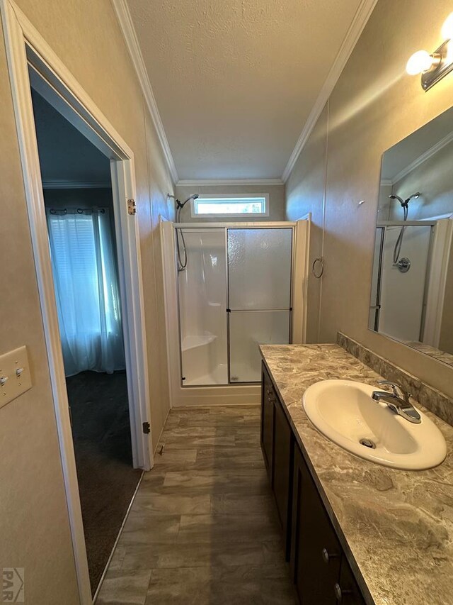 full bath with vanity, wood finished floors, a textured ceiling, crown molding, and a shower stall