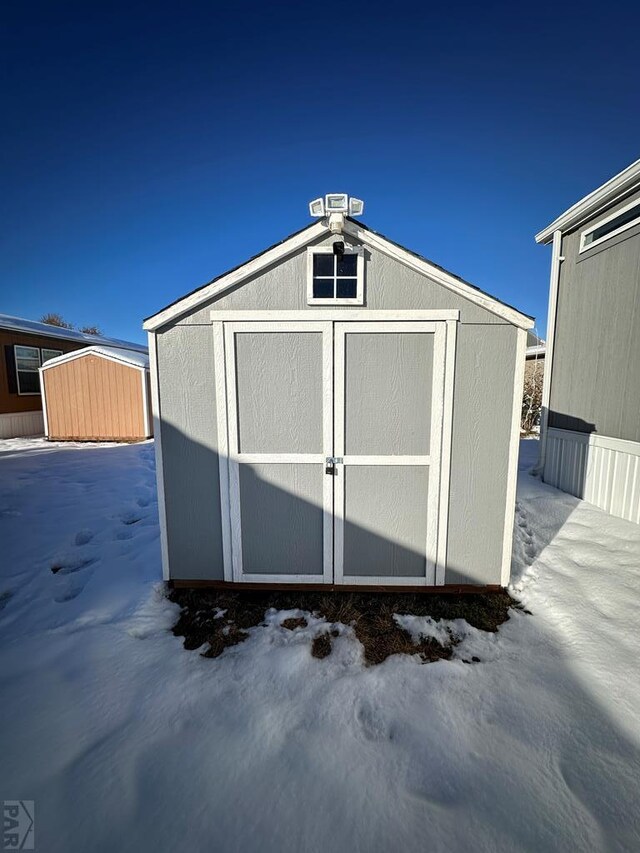 snow covered structure with a storage shed and an outdoor structure