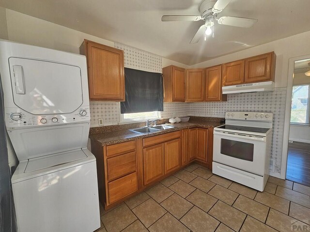 kitchen featuring under cabinet range hood, a sink, stacked washing maching and dryer, white range with electric stovetop, and dark countertops