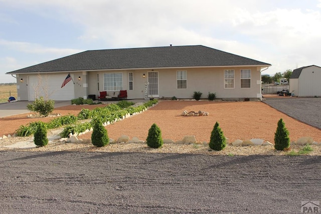 ranch-style house with concrete driveway, an outbuilding, an attached garage, a shed, and stucco siding