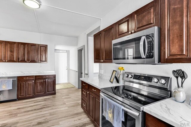kitchen with stainless steel appliances, dark brown cabinetry, light stone counters, and light wood finished floors