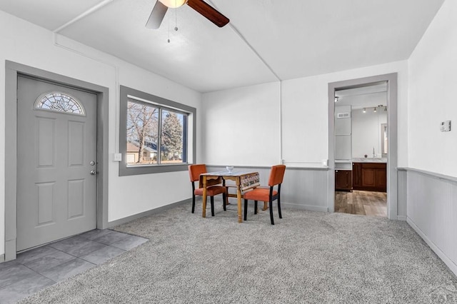 carpeted dining area featuring ceiling fan, wainscoting, and baseboards