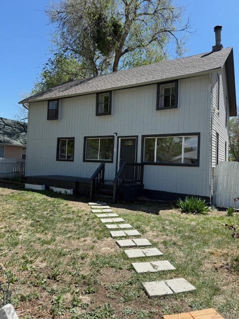 view of front facade featuring a shingled roof, fence, and a front yard