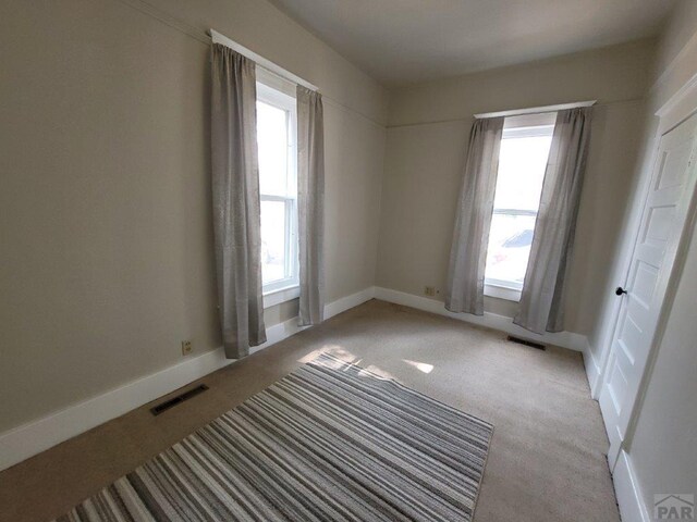 spare room with light colored carpet, visible vents, and baseboards