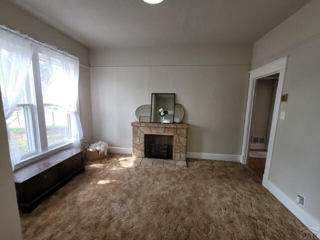 unfurnished living room with a stone fireplace, carpet, visible vents, and baseboards