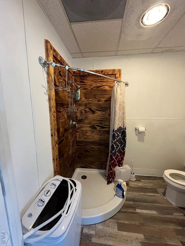 full bath with a drop ceiling, toilet, wood finished floors, baseboards, and a stall shower