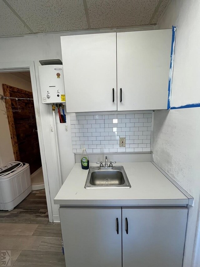 kitchen with tasteful backsplash, white cabinets, light countertops, a paneled ceiling, and a sink