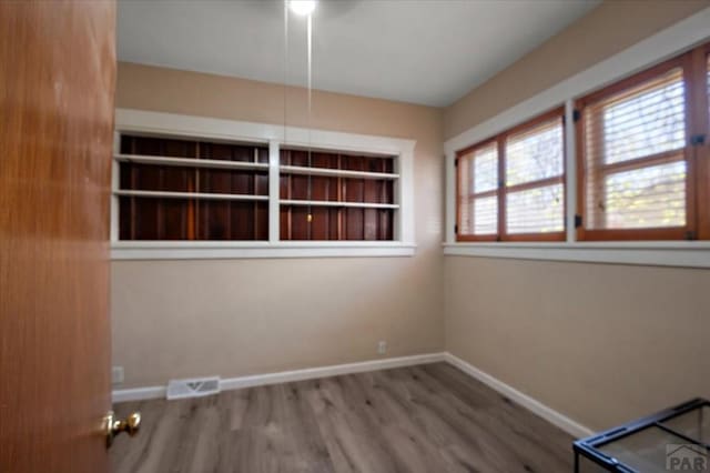 empty room featuring baseboards, wood finished floors, and visible vents