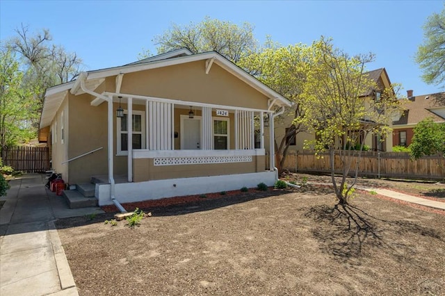 bungalow-style house with stucco siding, fence, covered porch, and driveway