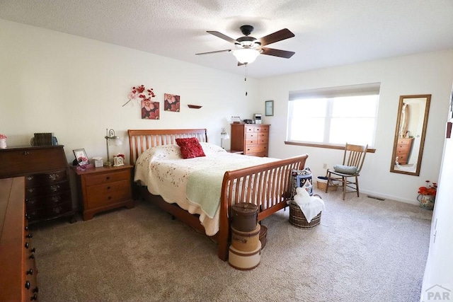 bedroom with a textured ceiling, dark carpet, visible vents, and a ceiling fan