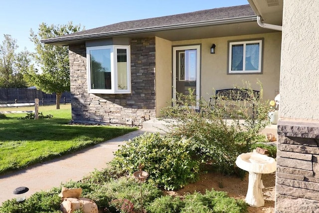 entrance to property with stone siding, a lawn, and stucco siding