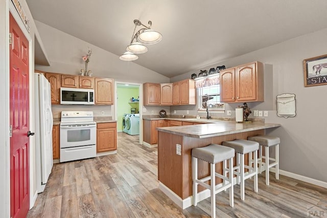 kitchen featuring light wood finished floors, washer and dryer, white appliances, a peninsula, and a kitchen bar